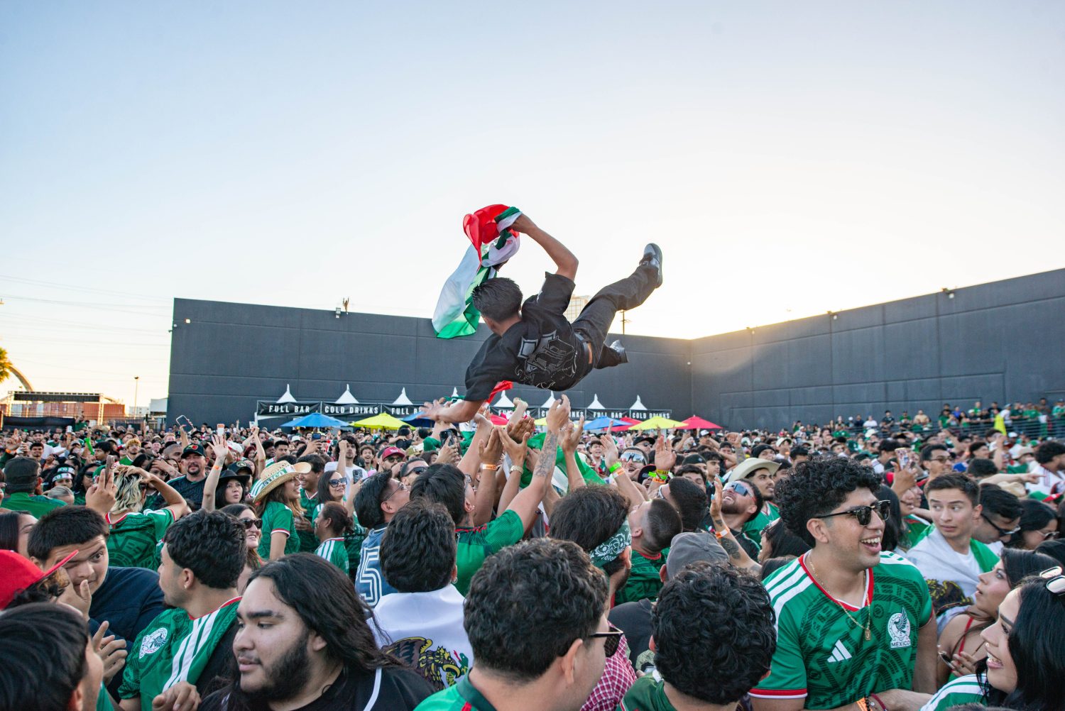 Crowd in Mexico jerseys crowd-surfing a fan holding a flag